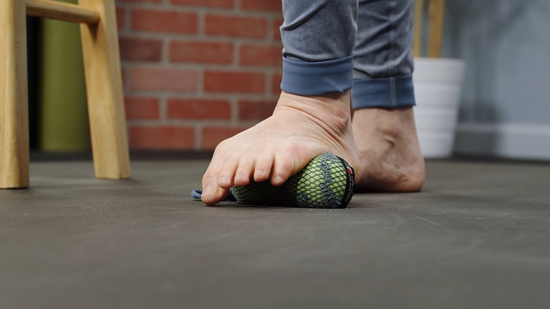 A person rolling their bare foot over a massage ball on the floor to target fascia in the sole