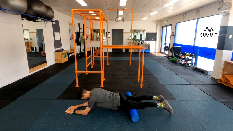 A man using a foam roller on his quads in a gym setting to release fascia tension in the front of the thighs