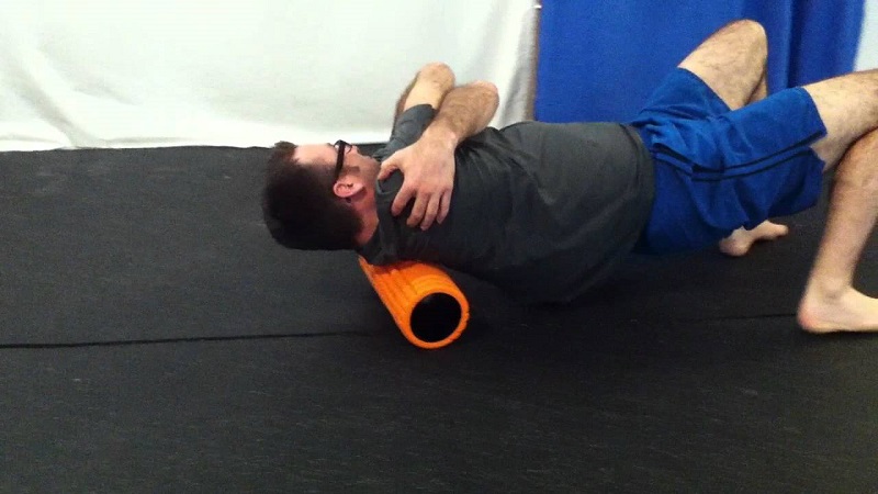 A man lying on a foam roller targeting his upper back and shoulder blades to relieve fascial tension