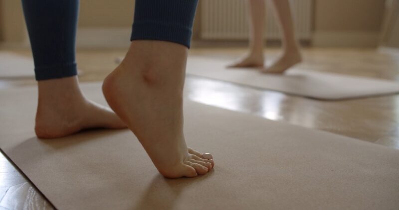 Close-up of bare feet performing a gentle calf raise on a yoga mat during a stretching session