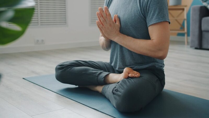 Man sitting in lotus position on a yoga mat with hands in prayer pose during a calm indoor yoga session