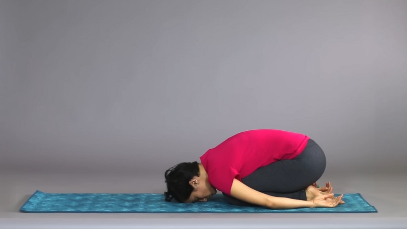 Person in Child's Pose (Balasana) resting on a yoga mat with arms relaxed and forehead touching the ground