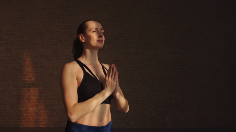 A woman stands with her hands in prayer position and eyes closed, practicing yoga to manage autoimmune flare-ups