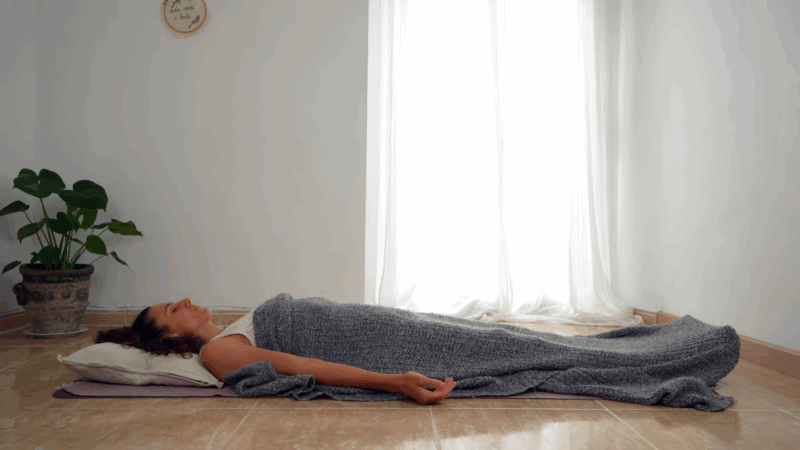 A woman lies on a mat covered with a blanket, resting peacefully during a Yoga Nidra session