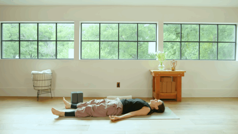 A woman lies on a yoga mat in a calm, bright room prepared for Yoga Nidra