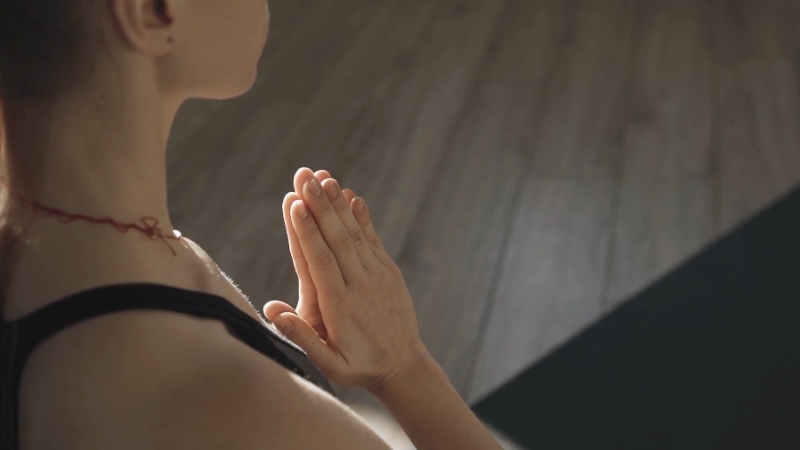A woman holds her hands in prayer position on a yoga mat to support her autoimmune health