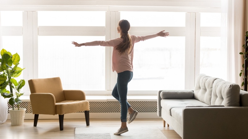 A woman opens her arms in a bright living room